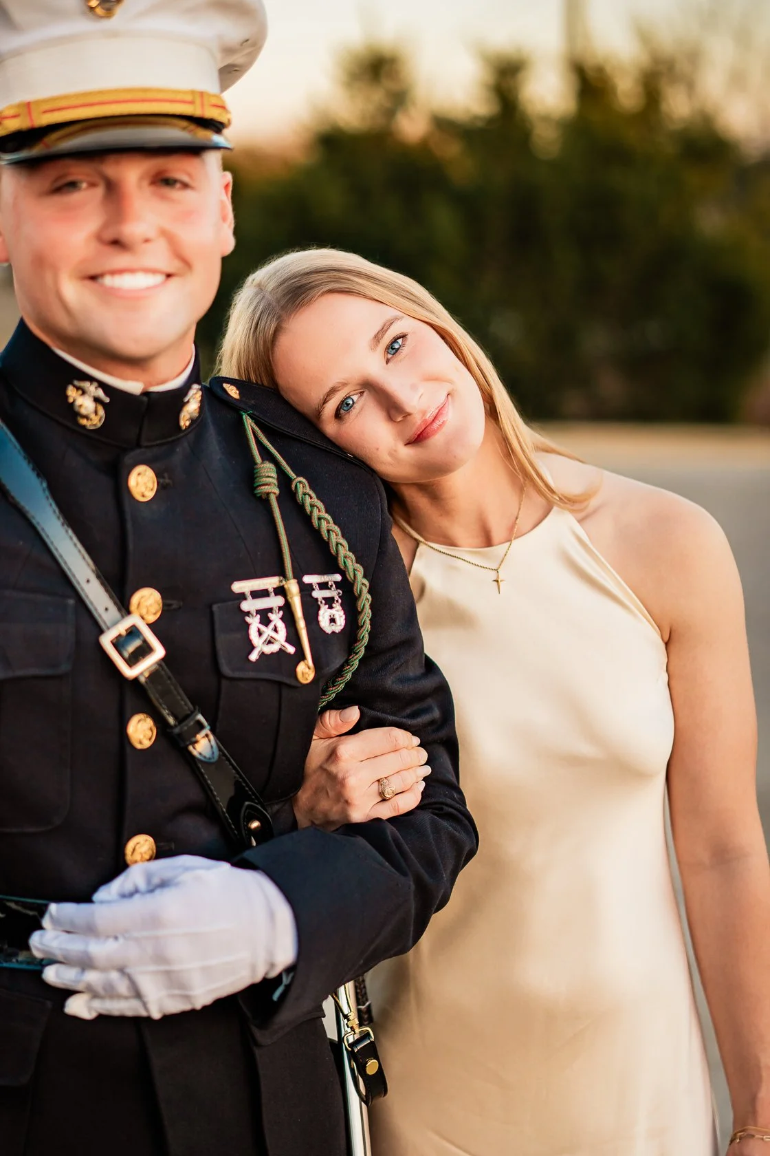 A woman with blonde hair and a man in a military uniform smiling together outdoors at sunset.
