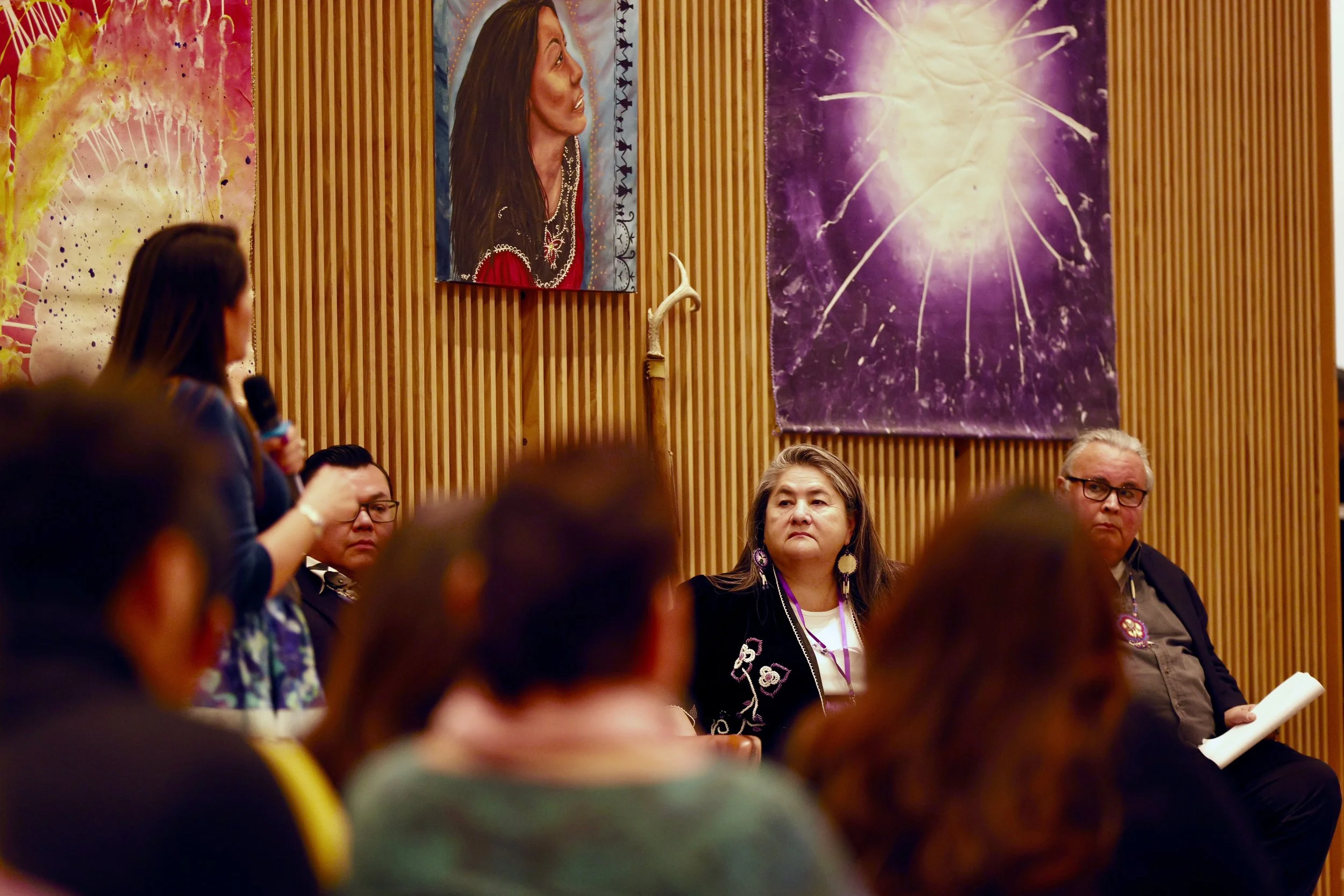 Kanien'kehá:ka Bear Clan Mother, Wakerahkáhtste Louise McDonald Herne, sits with other speakers as Michelle Shenandoah speaks at the 2025 Symposium.