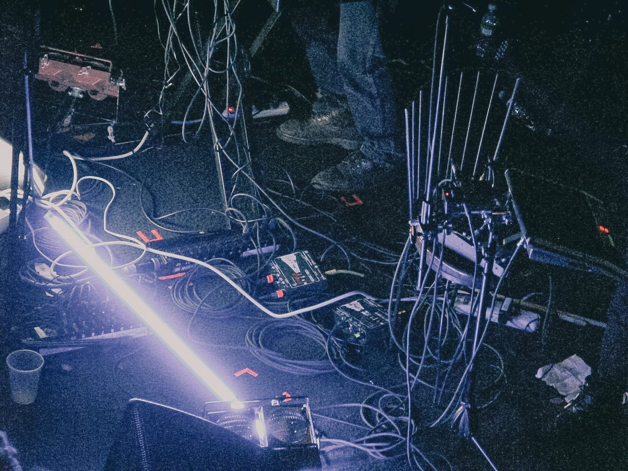 A DJ setup with turntables, mixers, and tangled cables illuminated by a bright white light in a dark environment.