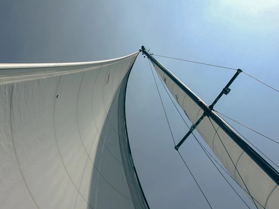Looking up at a sailboat's mast and sails against a clear blue sky