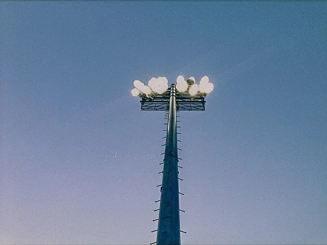 A tall blue communication tower with multiple white spherical antennas at the top against a clear blue sky.