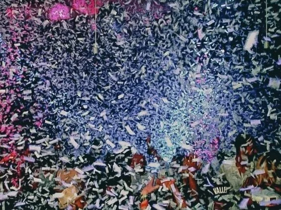 A concert crowd with confetti falling from above, illuminated by colorful stage lights.