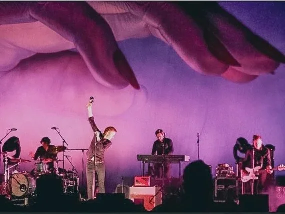 A band performing on stage with a backdrop of a large, stylized hand.