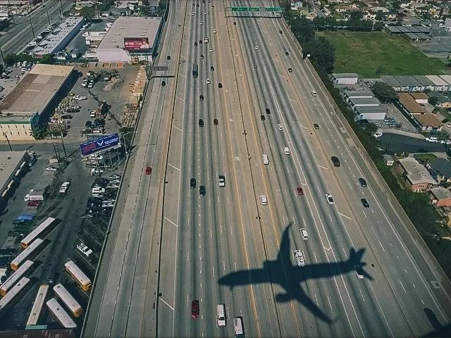 Aerial view of a highway with multiple lanes and cars, with the shadow of an airplane cast on the road.