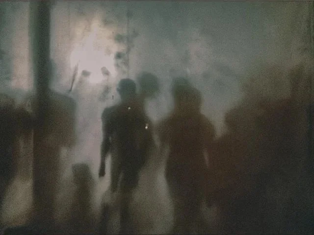 Three silhouetted figures walking through a smoky or foggy environment.