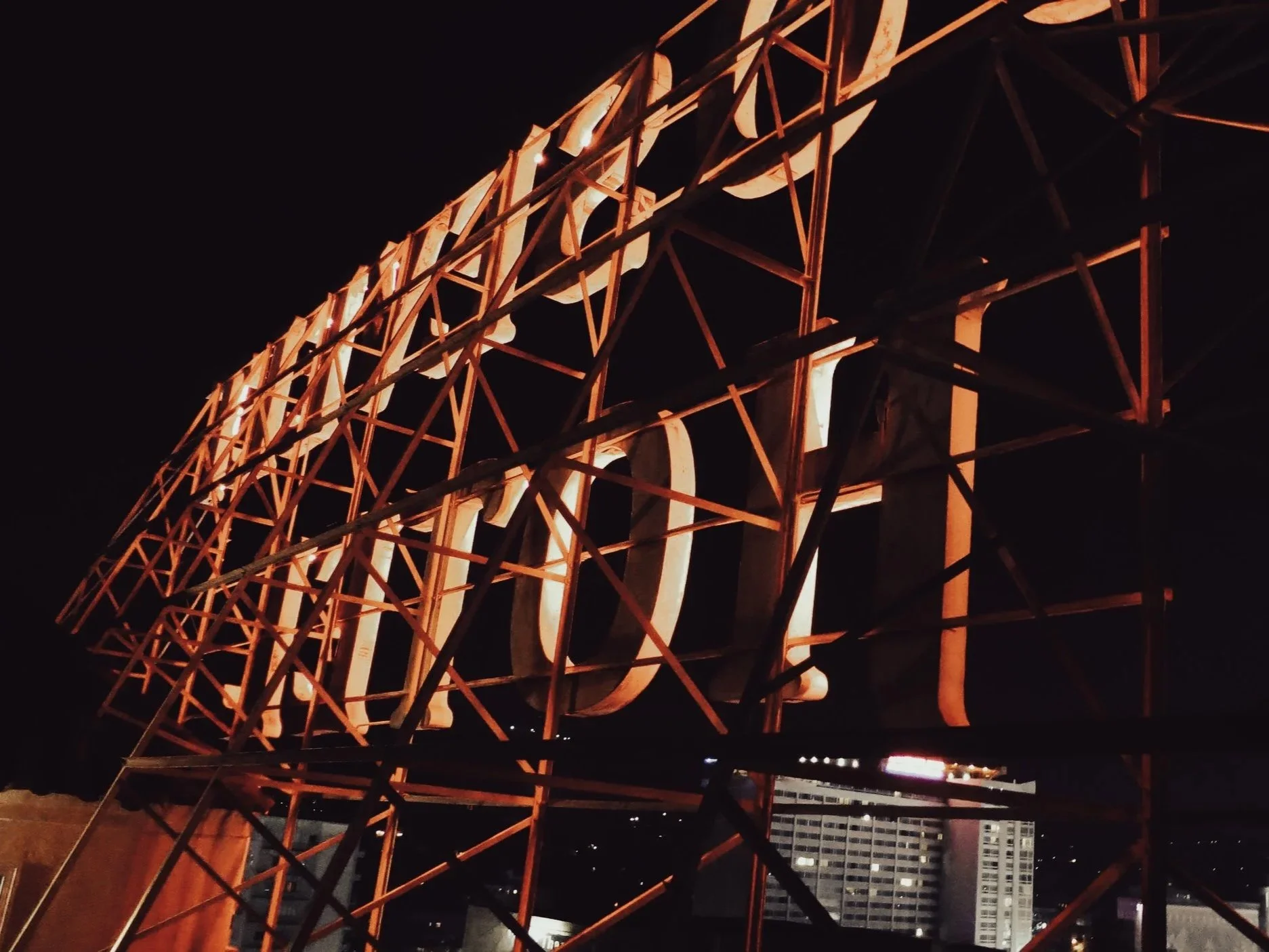Nighttime view of a large illuminated sign with the word 'Aloha' on an orange steel frame