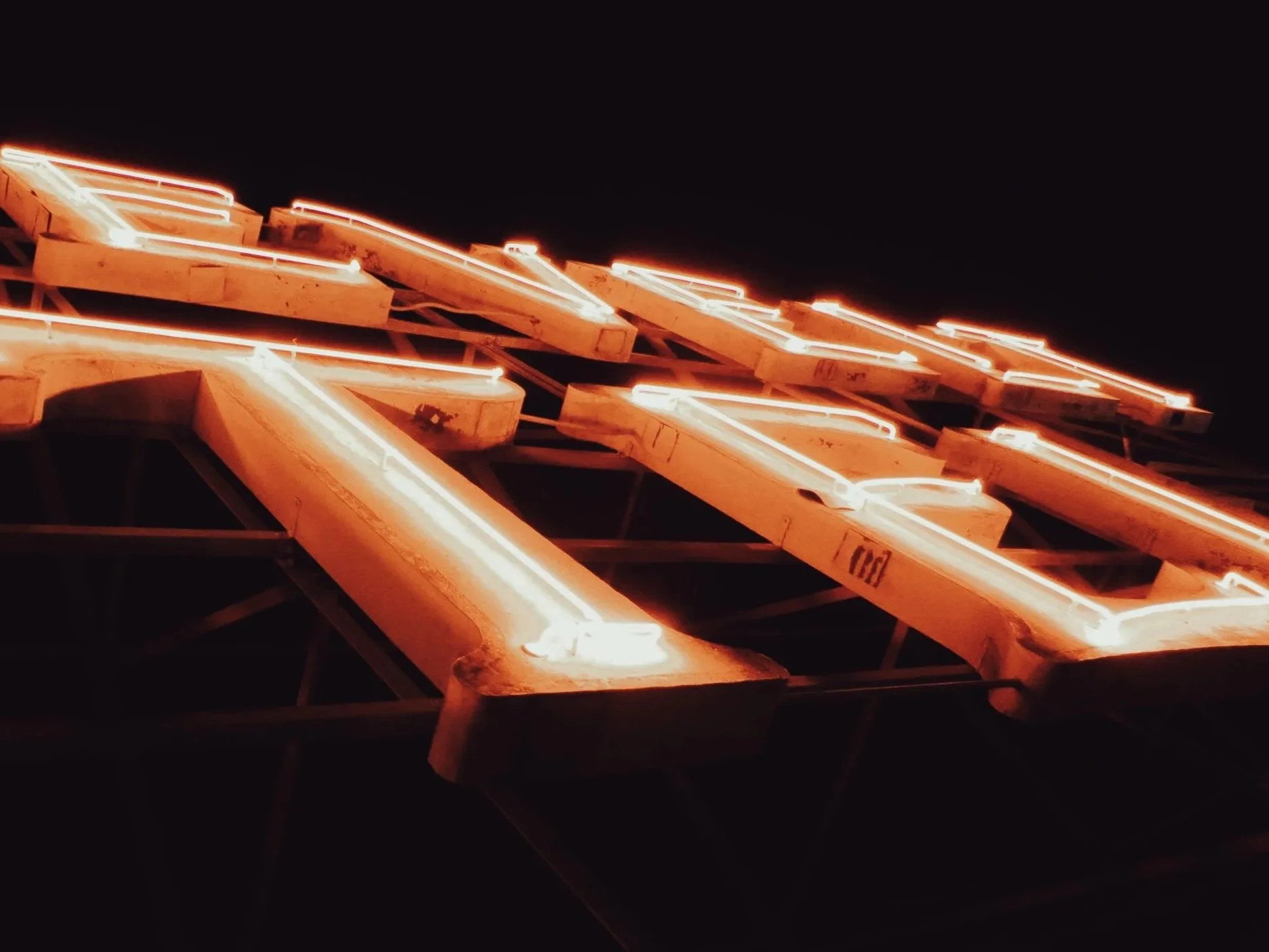 Close-up of illuminated neon lights in a stylized arrow shape against a dark background.