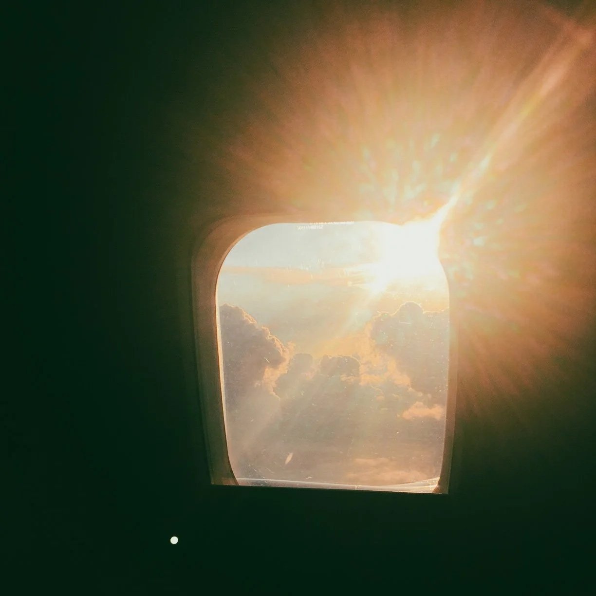 View of clouds and the sun shining through an airplane window.