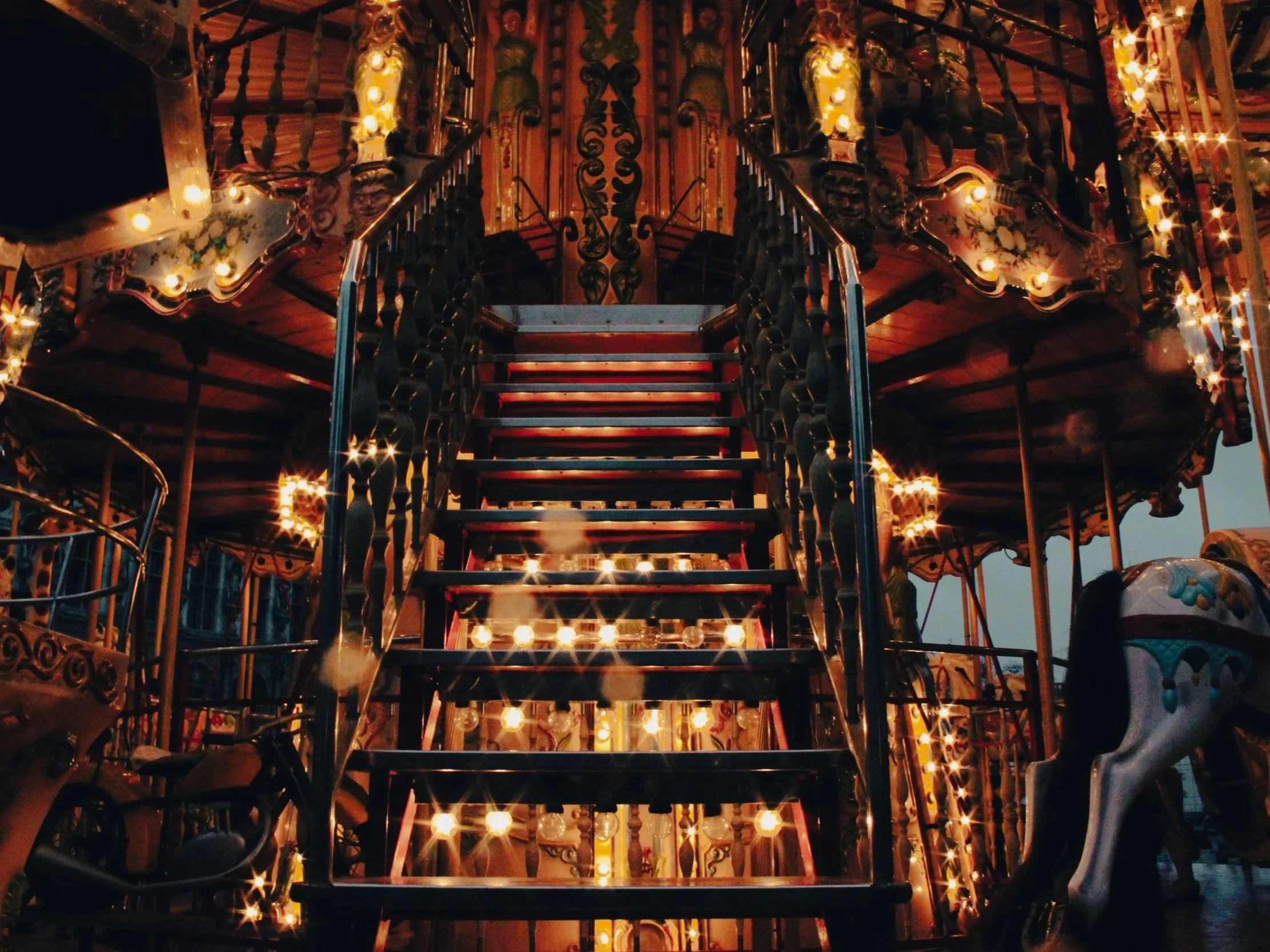 A vintage carousel at night with illuminated lights, featuring ornate wooden details and carousel horses.