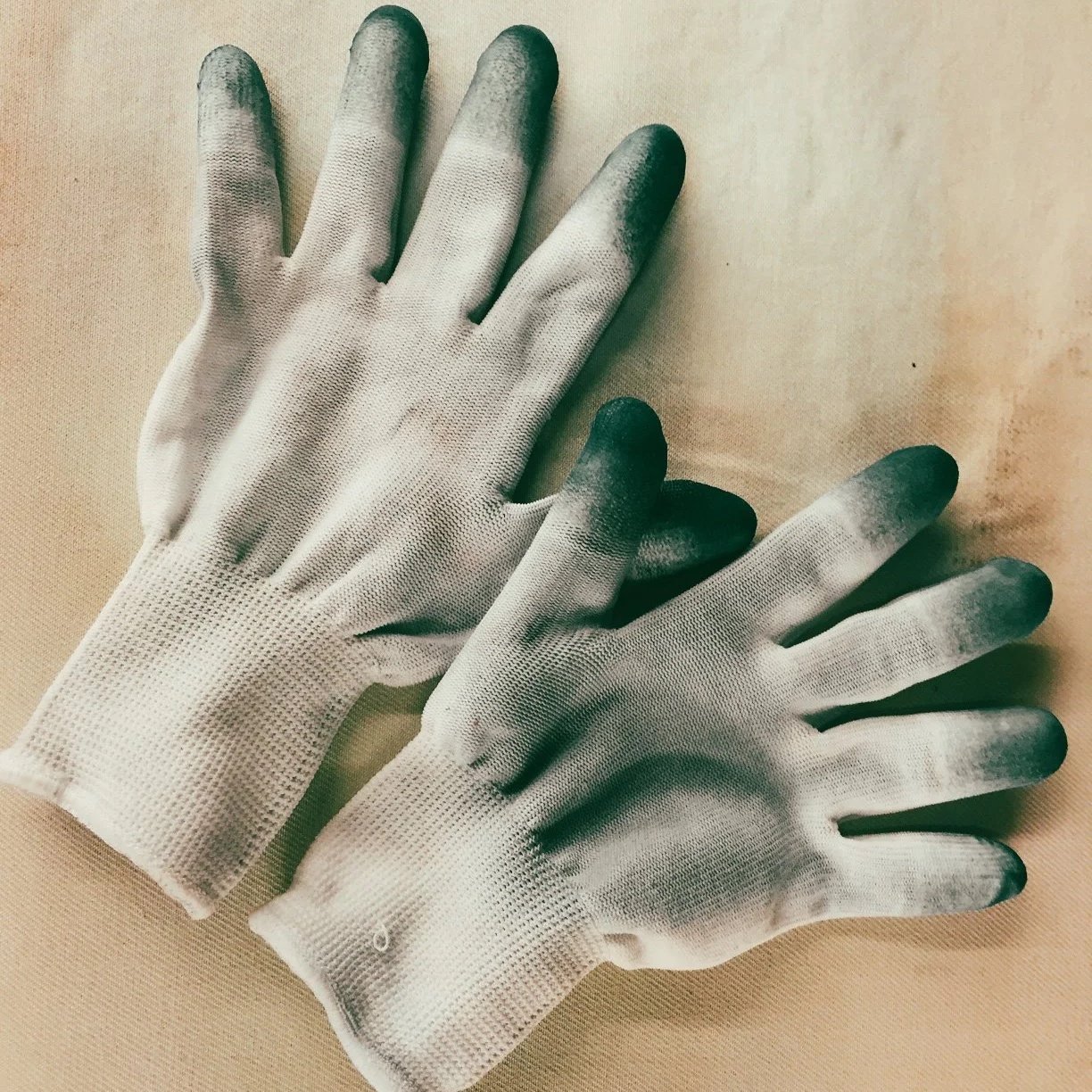 A pair of white work gloves with blackened fingertips resting on a beige surface.