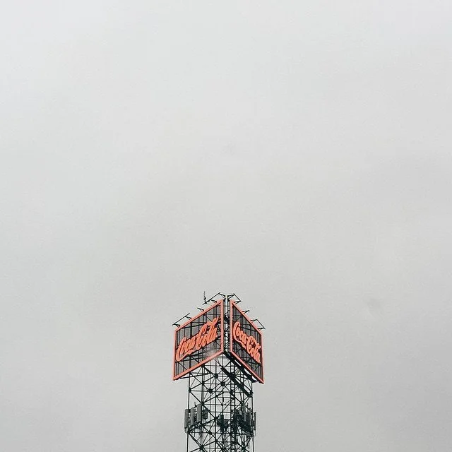 A Coca-Cola sign on a tall metal tower against a cloudy gray sky.