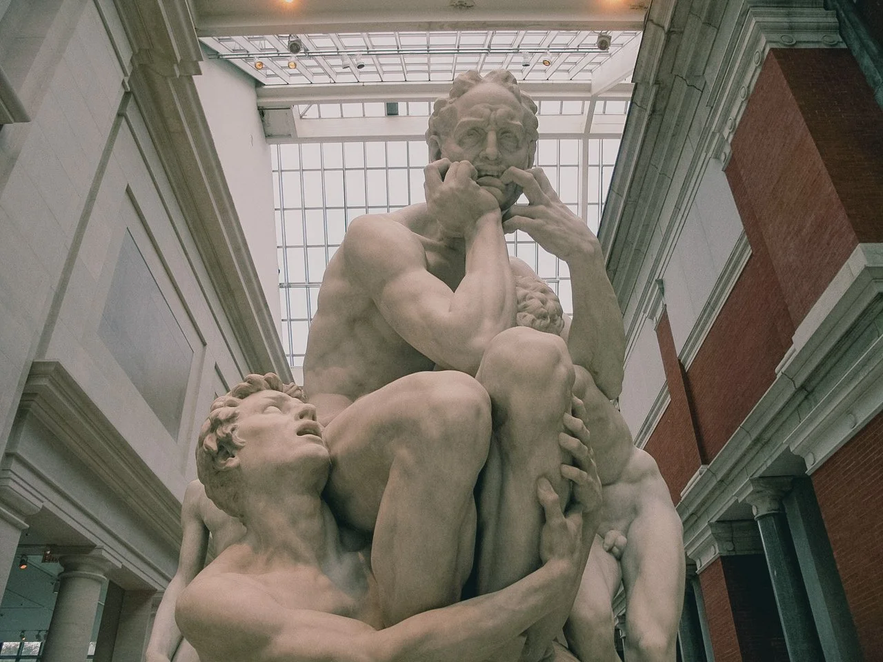 The sculpture represents a scene from Michelangelo's David, depicting a muscular man contemplating with several smaller human figures surrounding him in a historical museum setting.