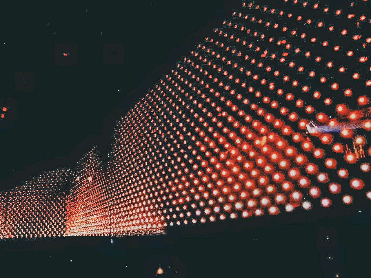 An artistic display of a large, curved wall covered in evenly spaced red lights against a dark background.