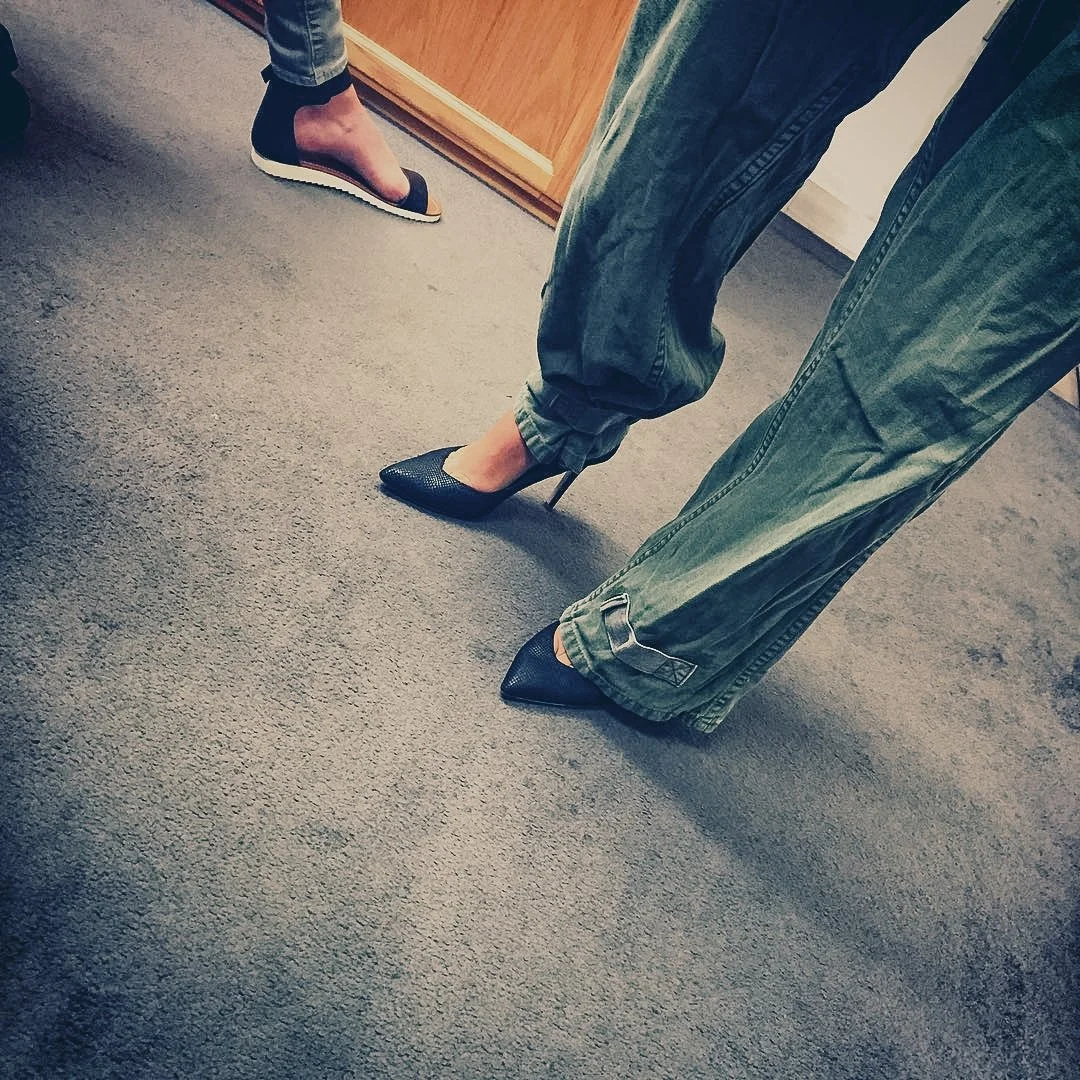People wearing high-heeled shoes and casual pants standing on a carpeted floor.