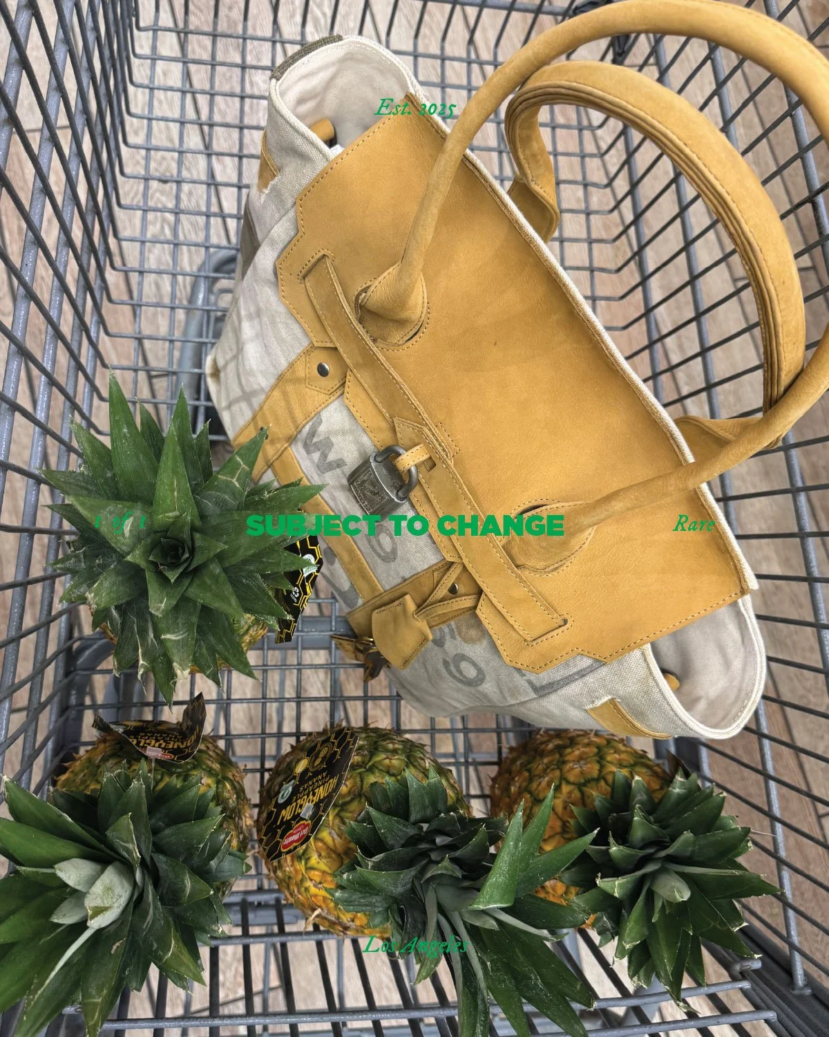 A shopping cart containing a beige and yellow handbag and four pineapples with green tops.