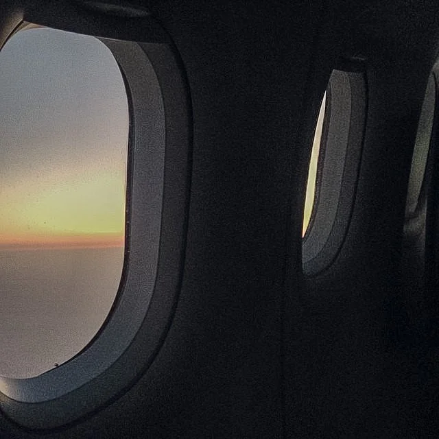 View from an airplane window showing a sunset or sunrise over the clouds.