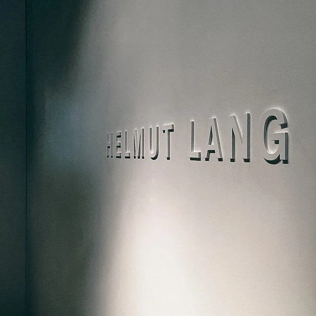 The image shows a wall with the name 'Helmut Lang' engraved in 3D letters.