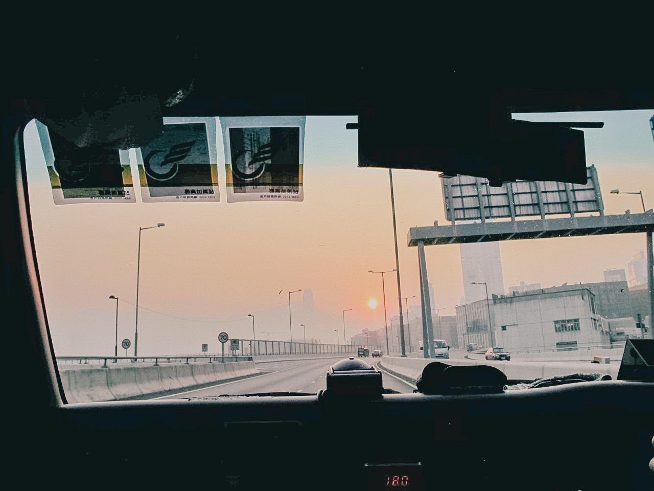 View from inside a vehicle on a highway at sunset, with a city skyline in the distance and several cars on the road.