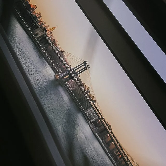 View of the Brooklyn Bridge and Manhattan skyline during sunset seen through a window.