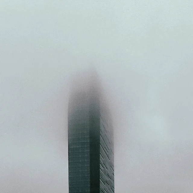 Tall modern skyscraper partially obscured by fog or low clouds.