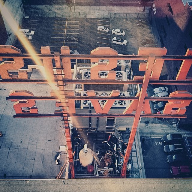 View of a rooftop with a large red sign spelling 'LOVE' from above, overlooking a parking lot with cars and a small outdoor gym area.