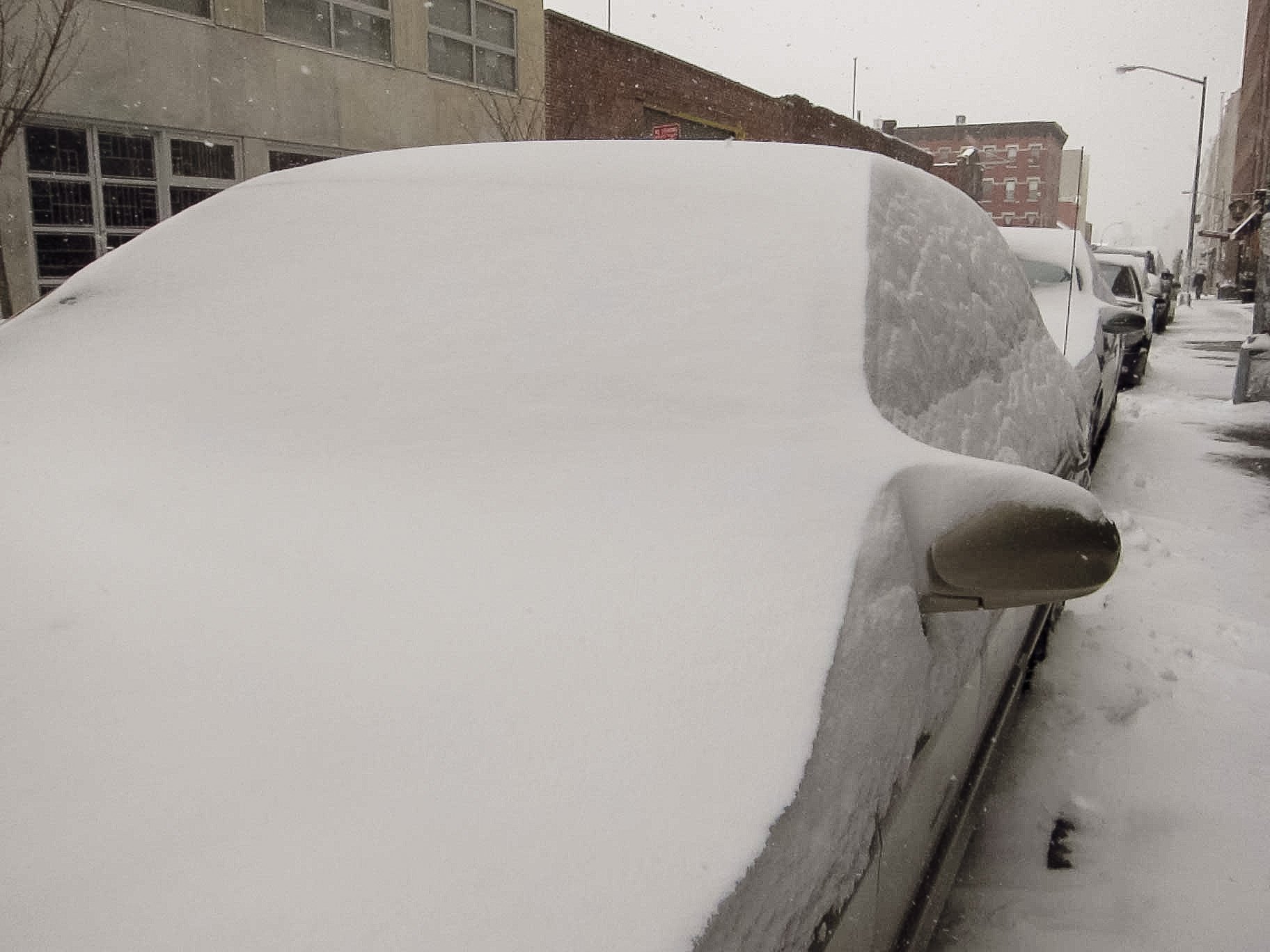 Car covered in snow parked on a city street during a snowstorm.