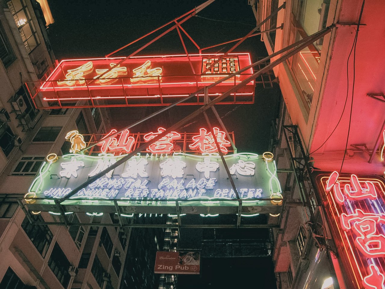 Neon signs for a restaurant named "Hing Chicken Restaurant Beer" and other businesses, illuminated at night in an urban area.