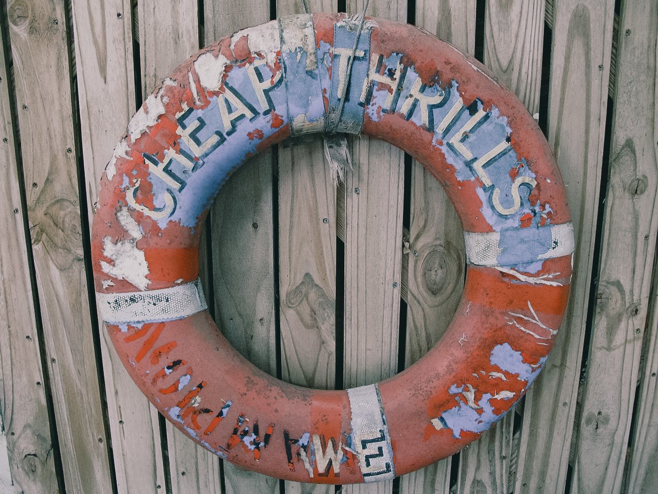 Weathered life preserver with peeling paint hanging on weathered wooden fence.