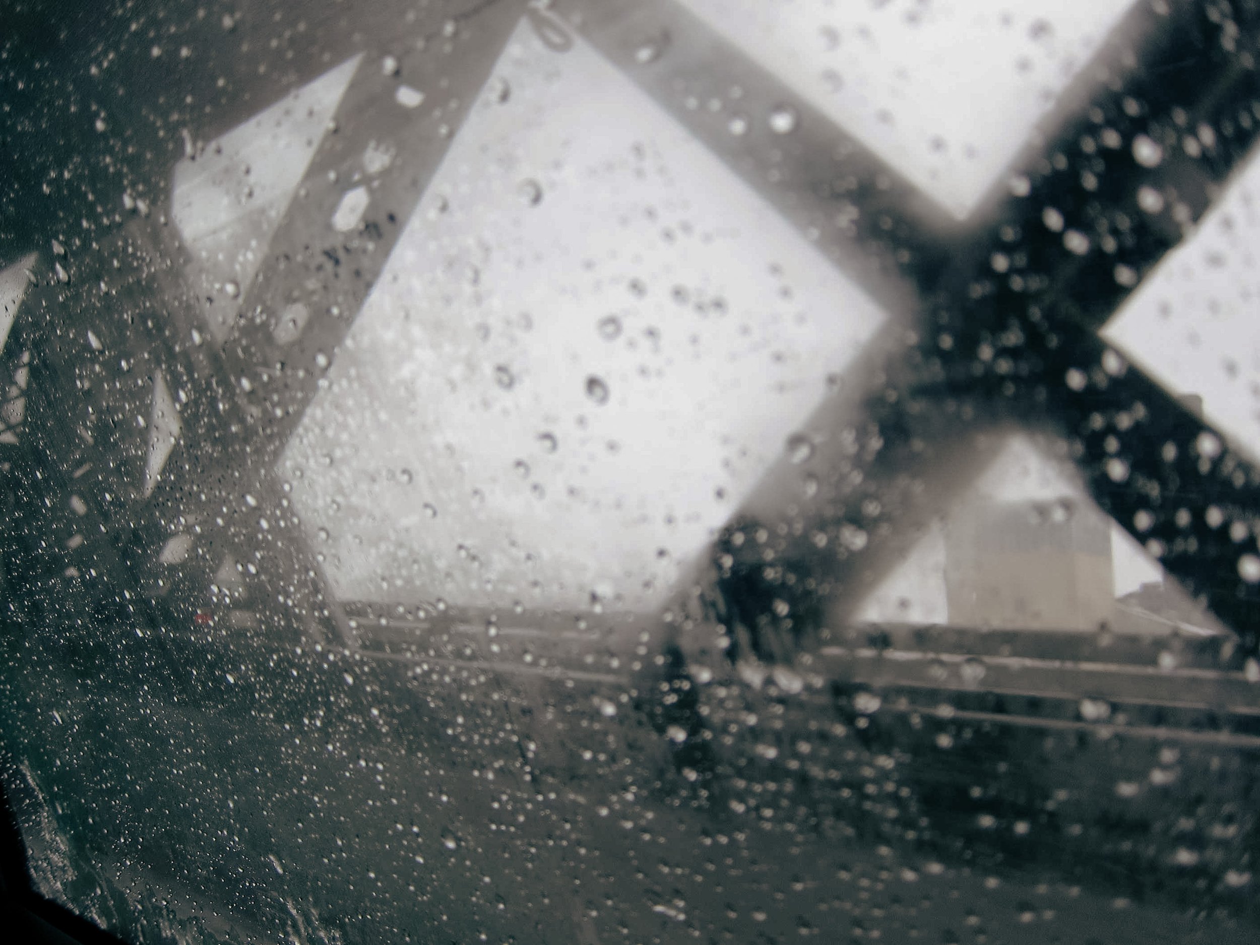 Rain-covered window with difficult to see through view of a bridge structure and the overcast sky