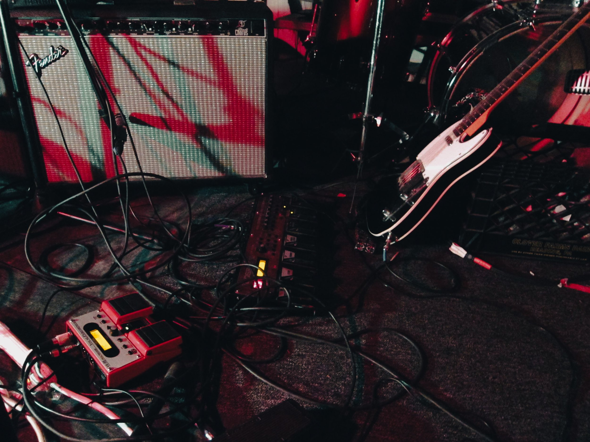 Musical equipment setup including an amplifier, guitar, pedals, and cables on a dark stage.