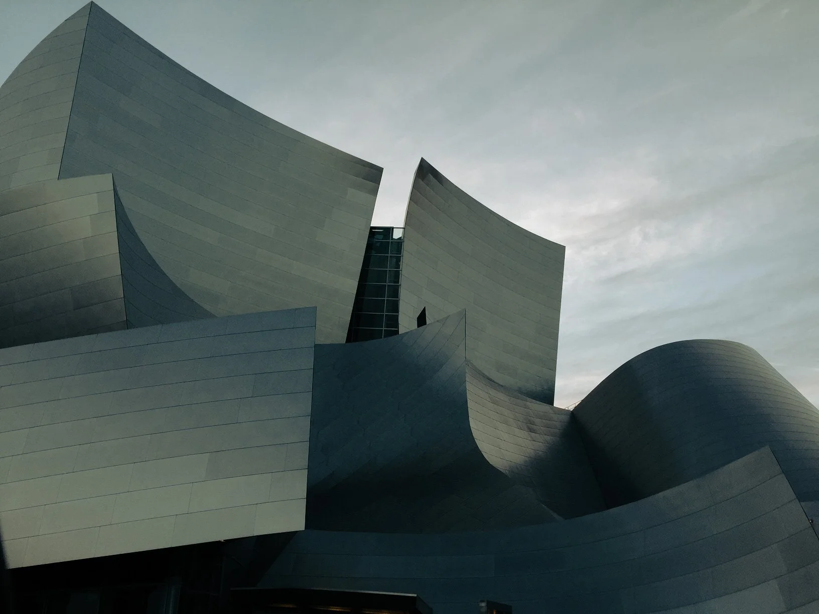 Modern building with curved metallic panels and dark glass windows under a cloudy sky.