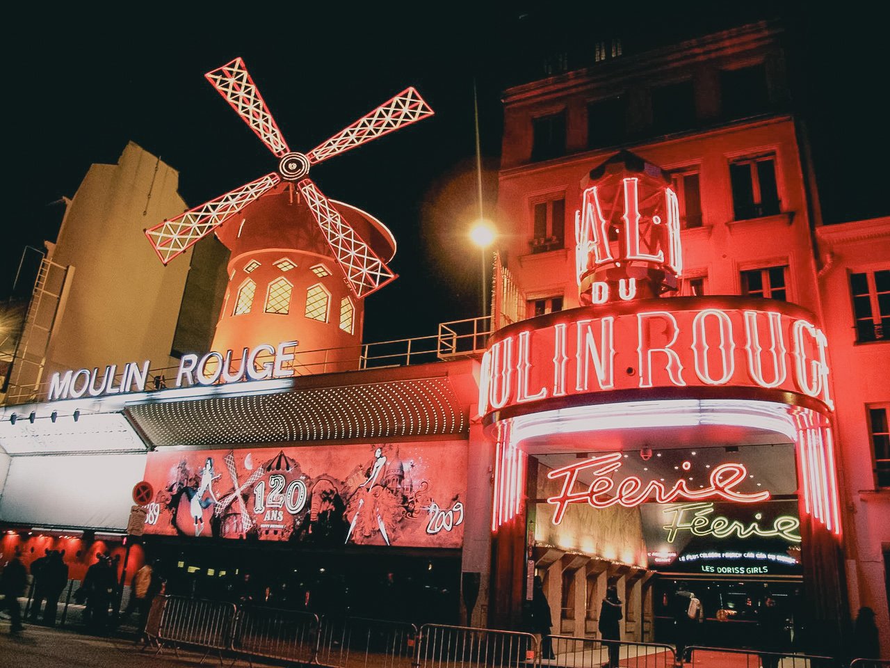 Night view of the Moulin Rouge cabaret in Paris with illuminated neon signs and a windmill on top.