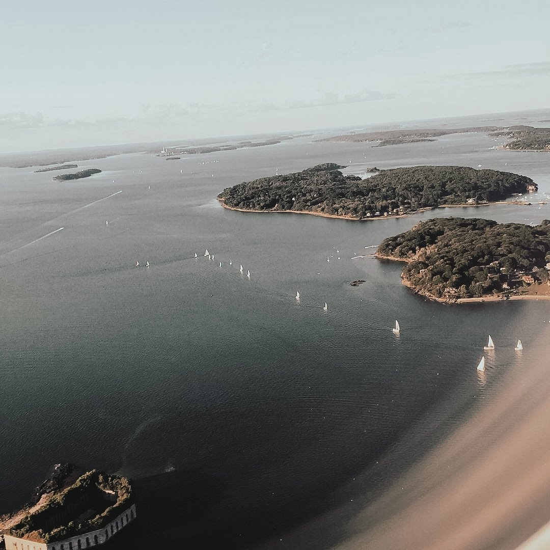 An aerial view of sailboats on a body of water surrounded by green, tree-covered islands.
