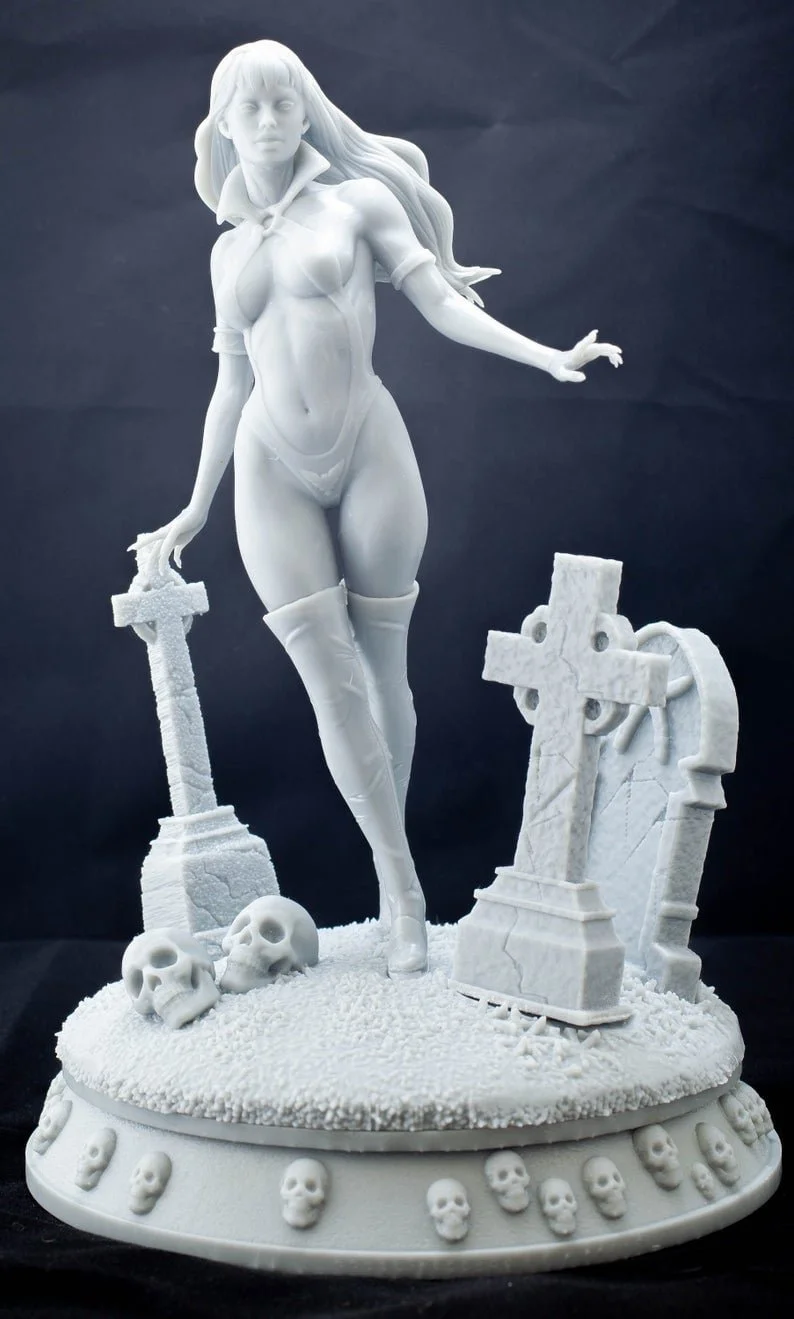 White sculpture of a female warrior standing on a tombstone surrounded by skulls, crosses, and grave markers, set against a dark background.