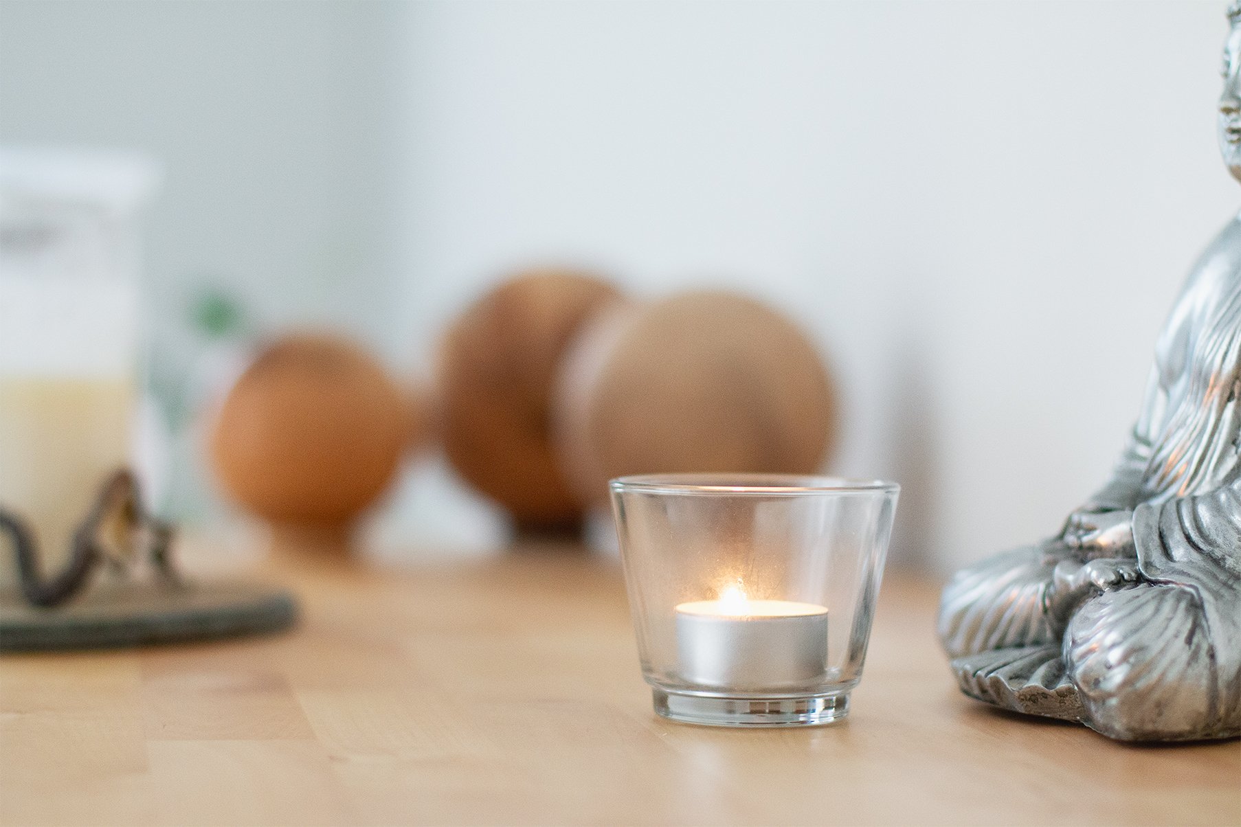 Eine brennende Kerze in einem kleinen Glas auf einem Holztisch, im Hintergrund Eier und andere Haushaltsgegenstände.