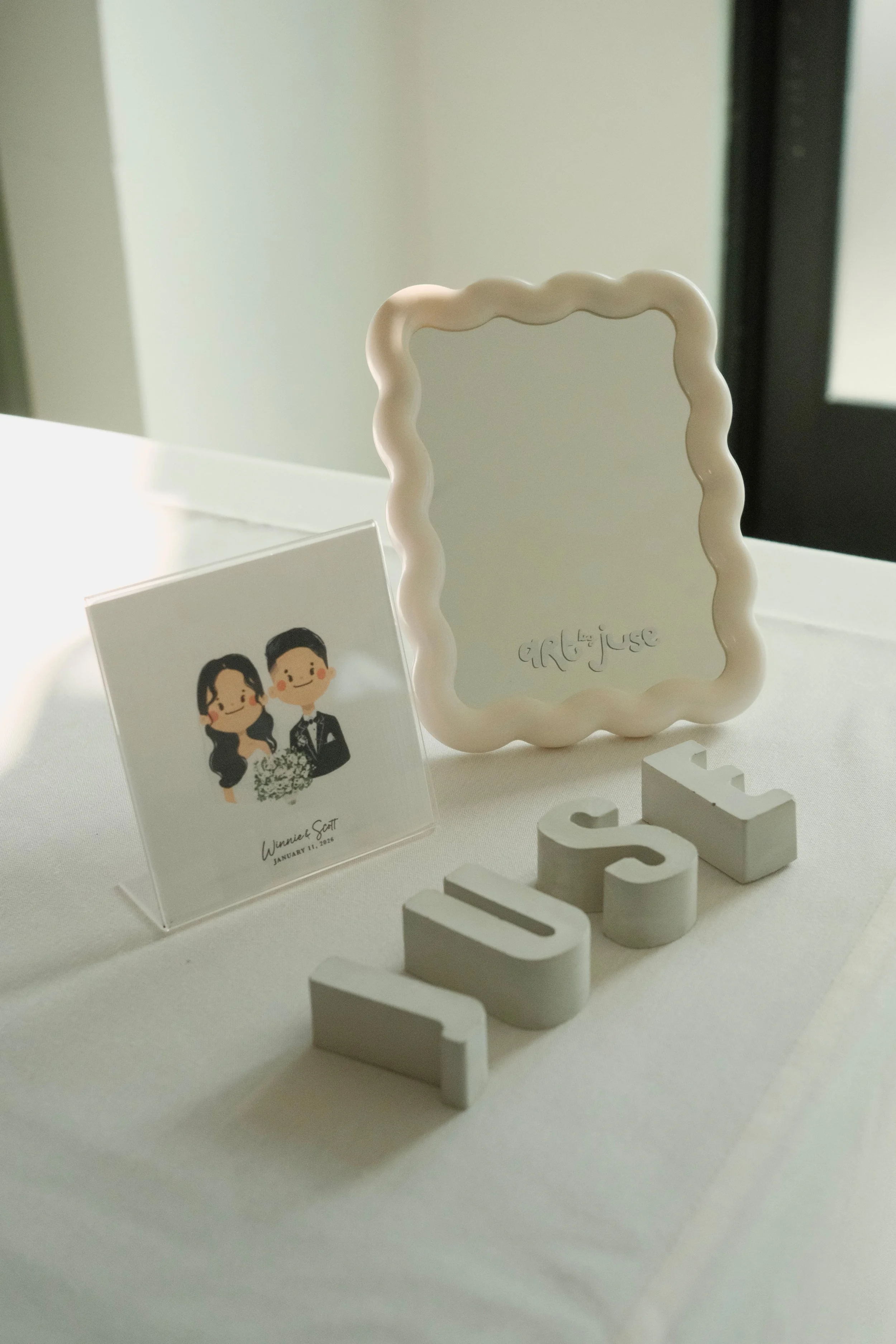 Decorative table display with a framed mirror, a small illustrated photo of a bride and groom, white letter blocks spelling 'LOVE', and a white stand with the phrase 'girl boss' engraved.