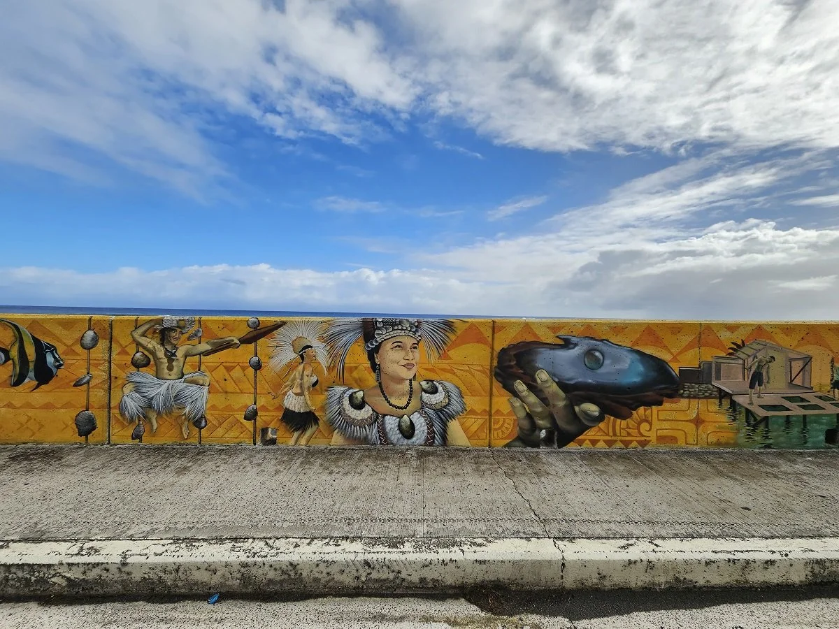 Straßenkunst mit träumerischer Frau in traditioneller Kleidung, einer Hand, die einen Fisch hält, und einer Person, die auf einer Plattform steht, vor einem blauen Himmel mit Wolken.