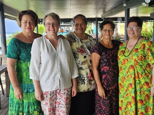 Katja Dorothea Buck und vier Frauen aus Vanuatu stehen nebeneinander auf einer Veranda mit Blick aufs Meer, alle lächeln und tragen bunte Kleider.