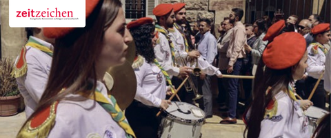 Syrische Christen traditionellen Trachten bei einer Parade, einige spielen Trommeln, im Hintergrund Menschenmenge und Gebäude.