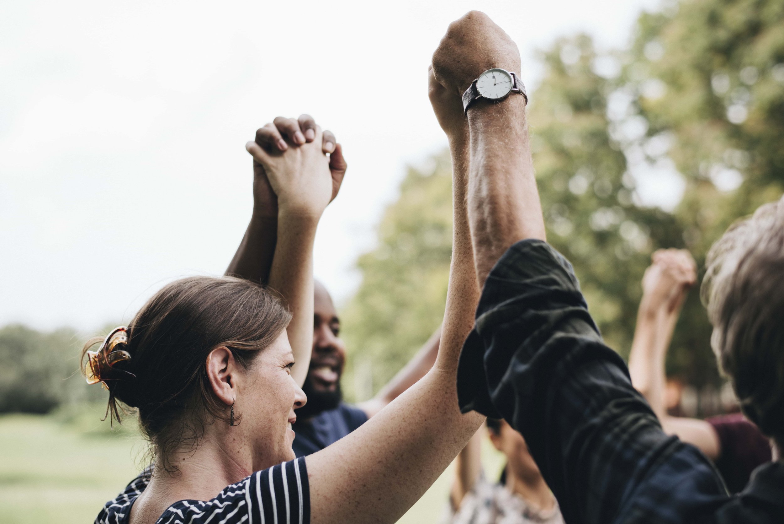 Group of diverse people celebrating outdoors with their hands raised and holding hands together.