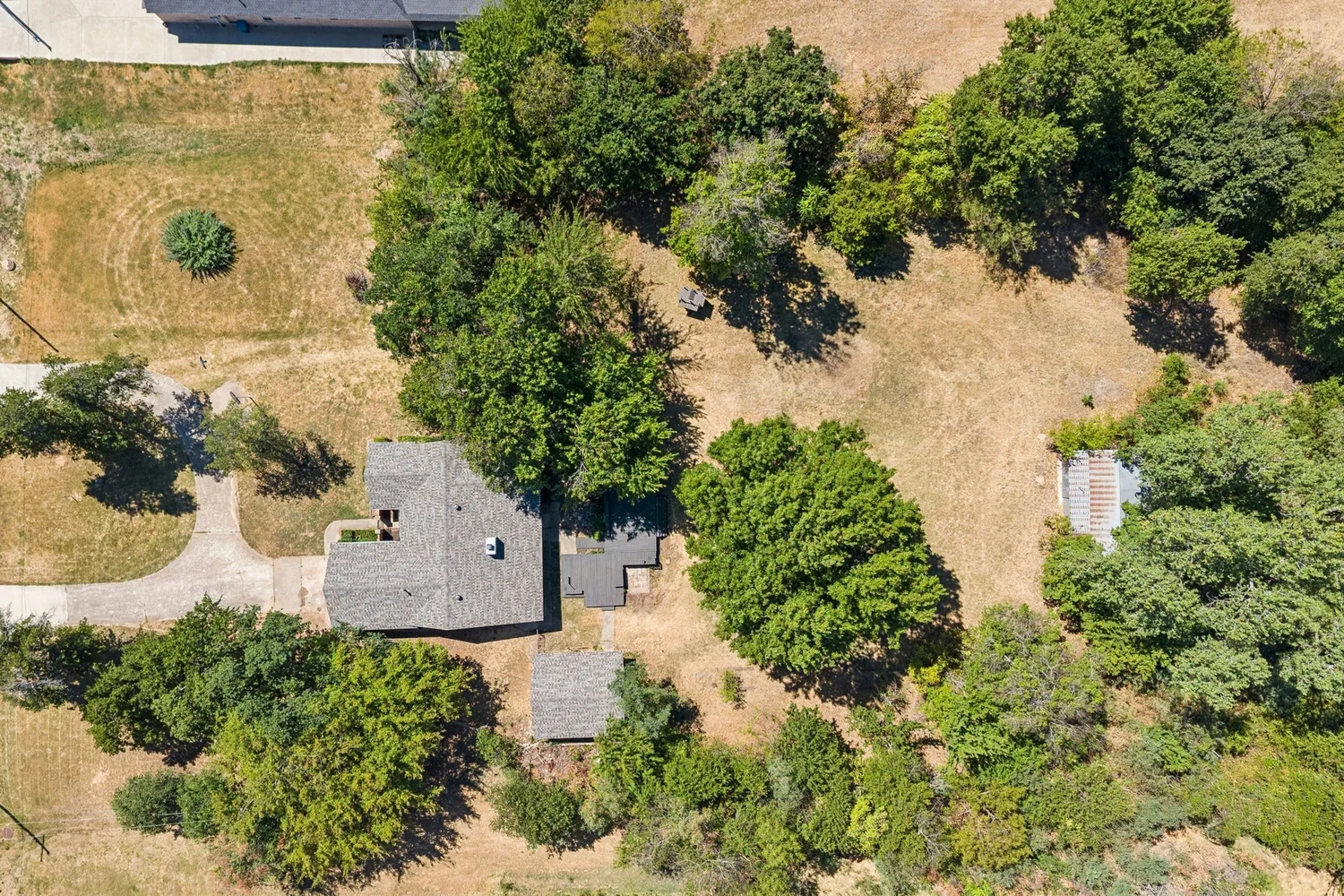 Overhead drone frame showing the roof line, outbuildings and tree canopy