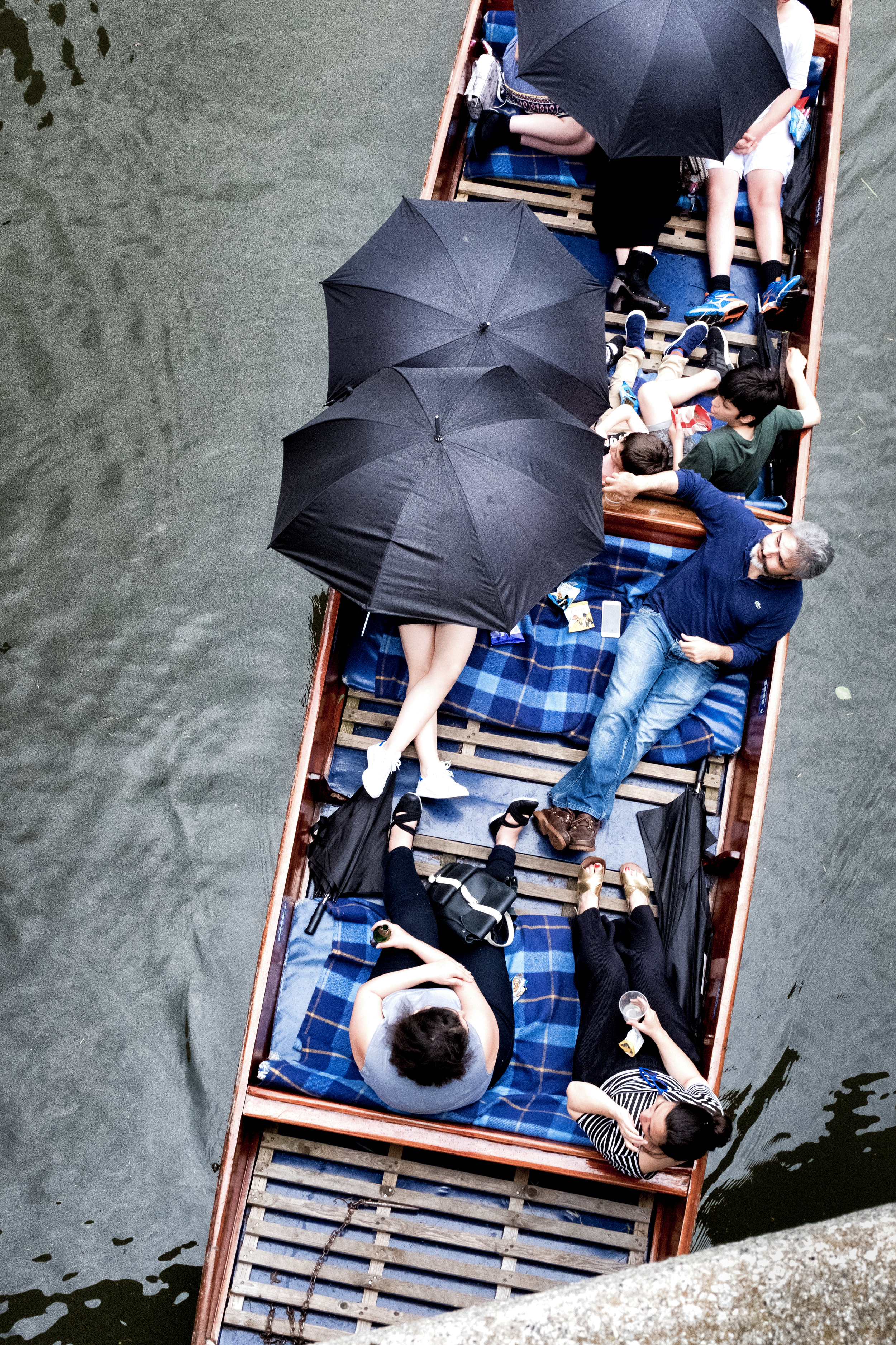 People relaxing on a boat with black umbrellas on a river.
