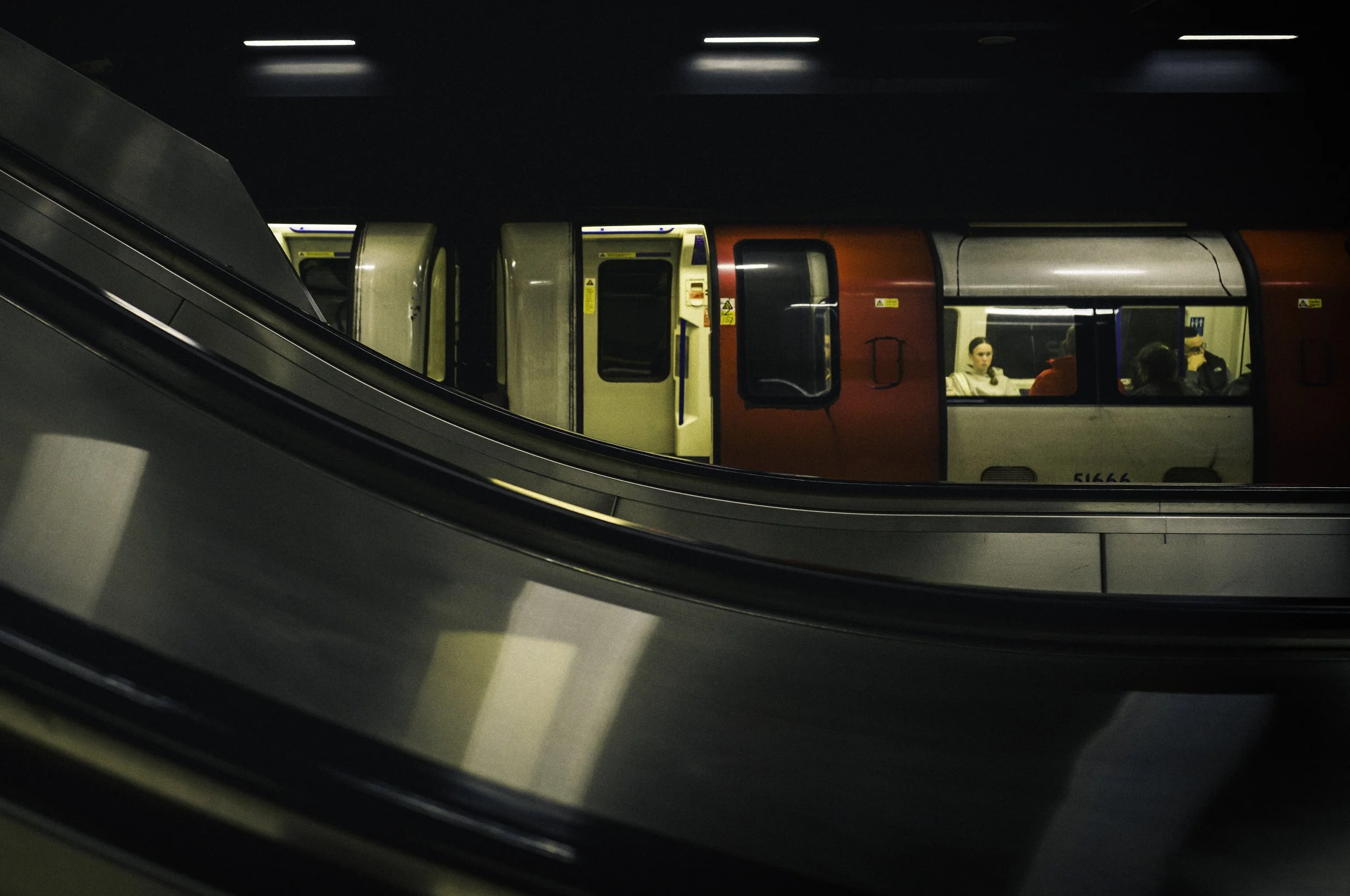 People sitting inside a subway train seen through an open door, with a moving walkway in the foreground.