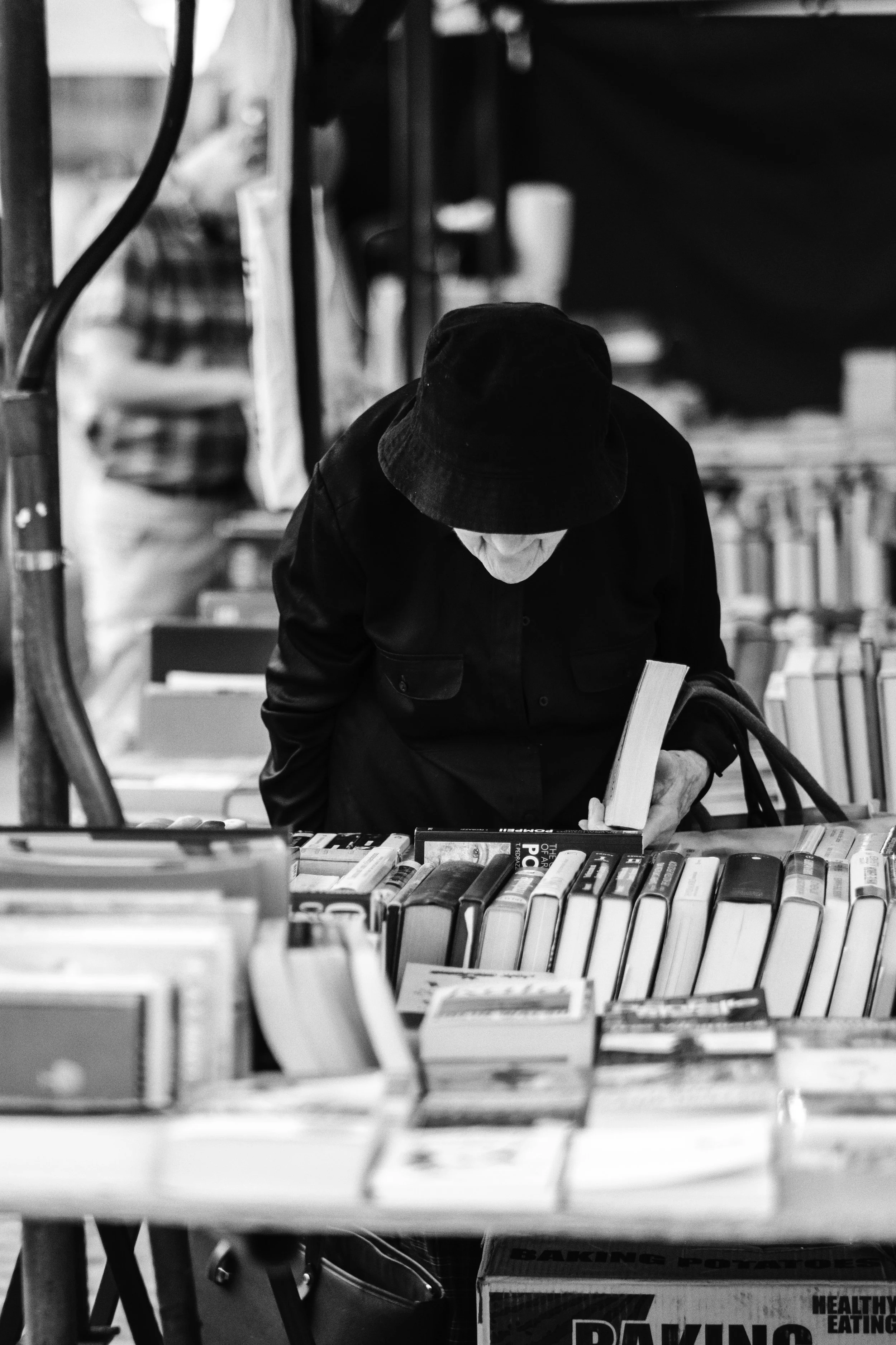 A person shopping at a bookstore, browsing through the books on a table, wearing a dark jacket and a bucket hat.