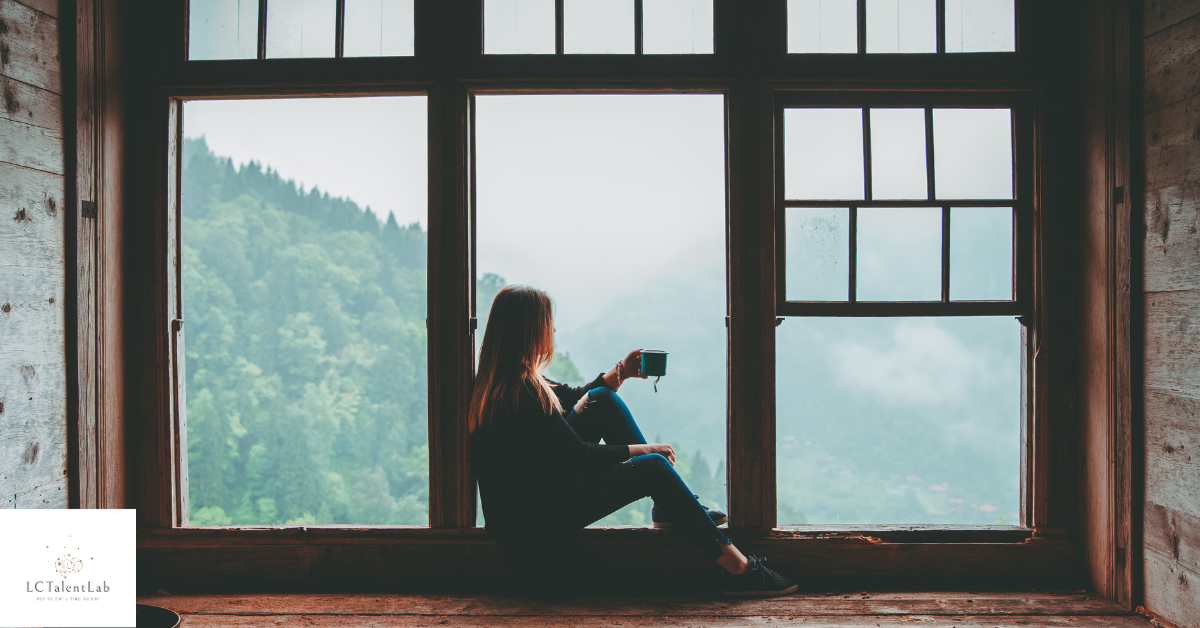 women sitting in a window looking at a forest