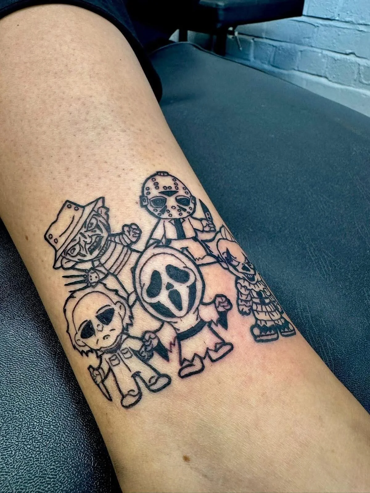 Tattoo of four cartoon characters from the Halloween series, including Michael Myers and other holiday-themed characters, on a person's lower leg.