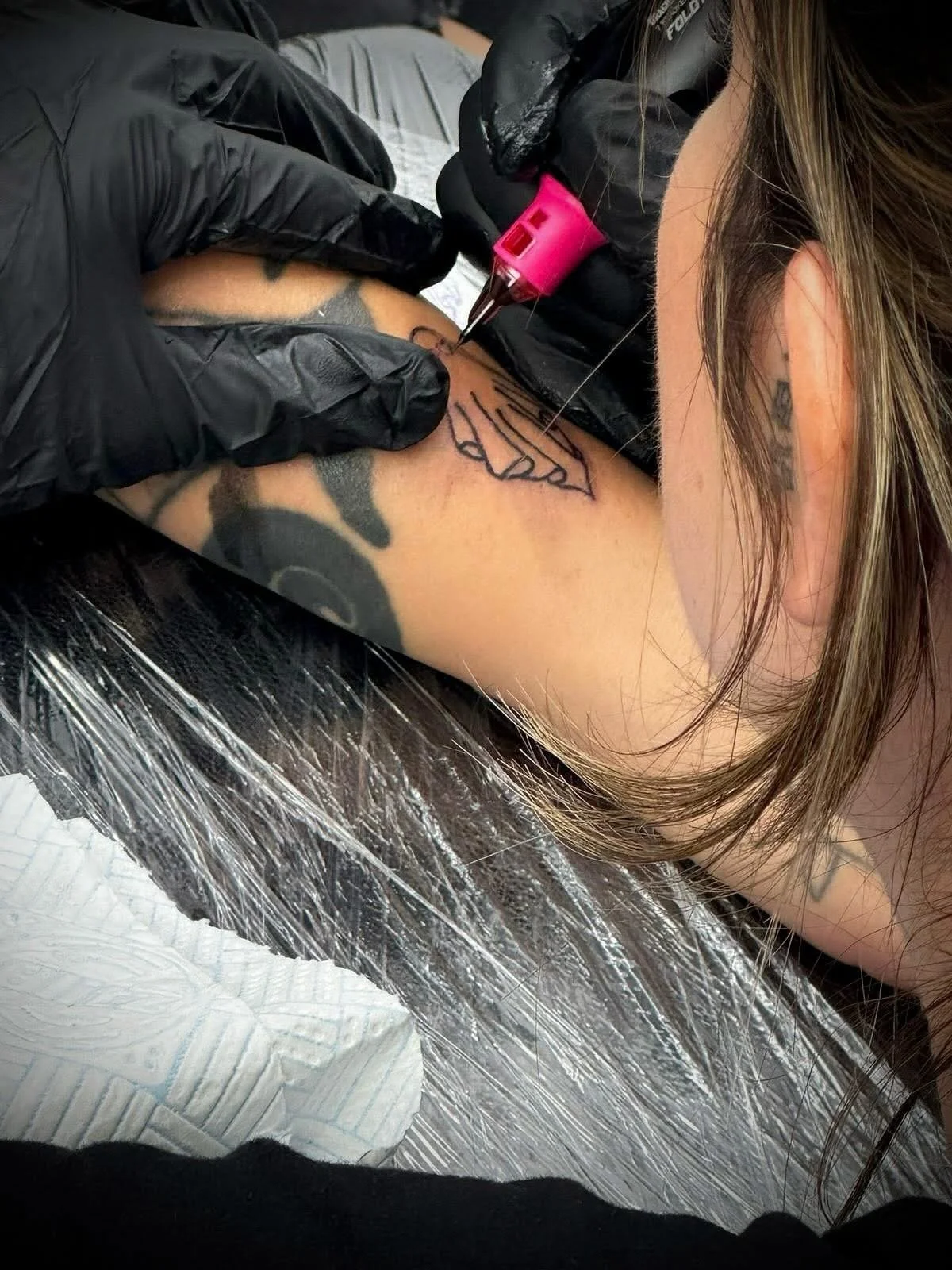 Tattoo artist using a needle and ink to create a tattoo on a person's shoulder, with another tattoo visible on the arm.