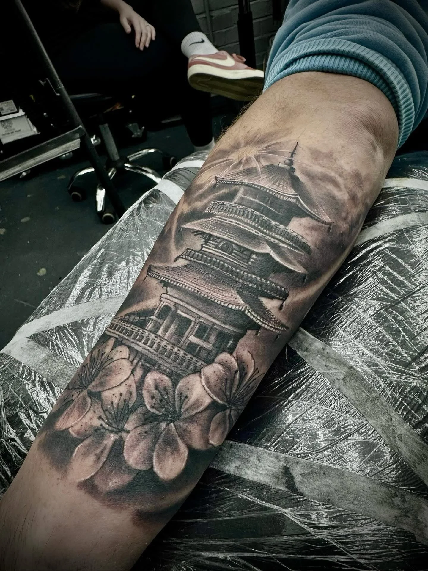 Tattoo of a traditional Japanese pagoda and cherry blossoms on someone's forearm.