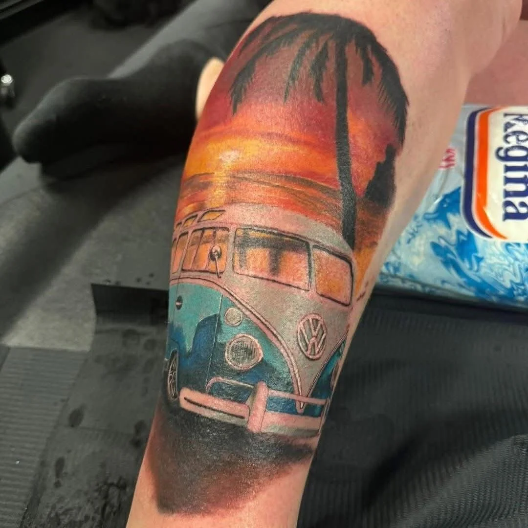 Tattoo of a vintage turquoise Volkswagen van parked under a sunset with palm trees.