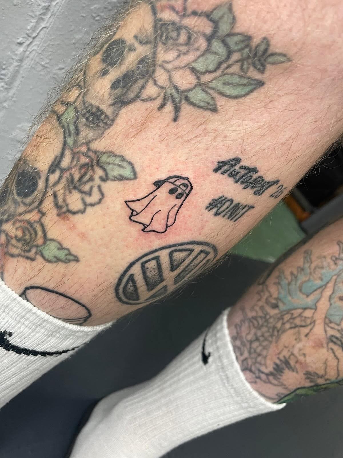 Tattoo of a ghost with a sheet and two eyes, accompanied by the text 'Feeling Ghost' and a peace symbol on a person's arm.